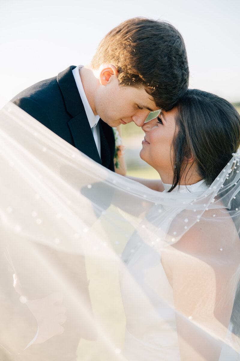 bride and groom looking at each other lovingly while wrapped in the bride's veil