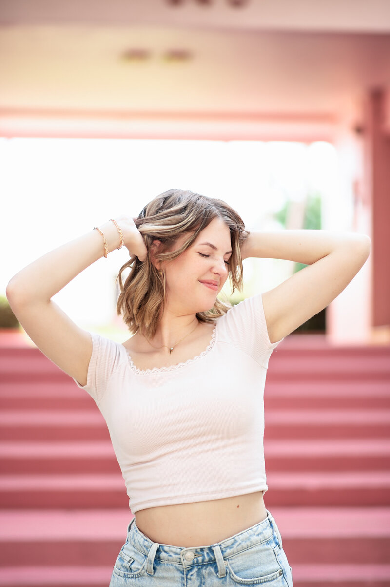 high school senior girl playing with hair in front of iconic pink apartment building in Winter Park