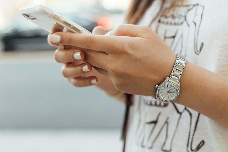 A close up of a woman's hand from the sideview clasping a phone and scrolling