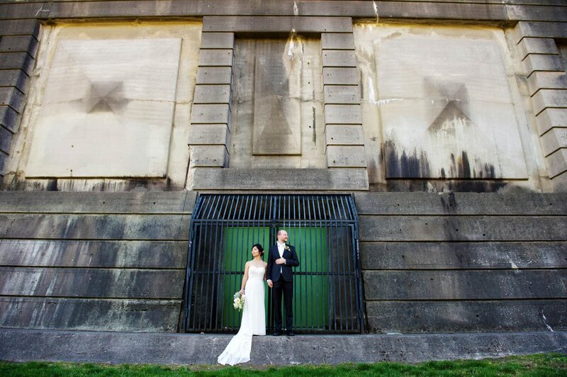 a bride and groom hold hands standing on the  base of st. johns bridge in cathedral park