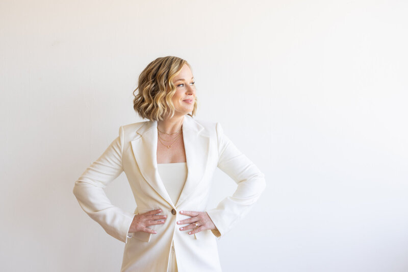 Lis in a white suit against a white wall looking to the side