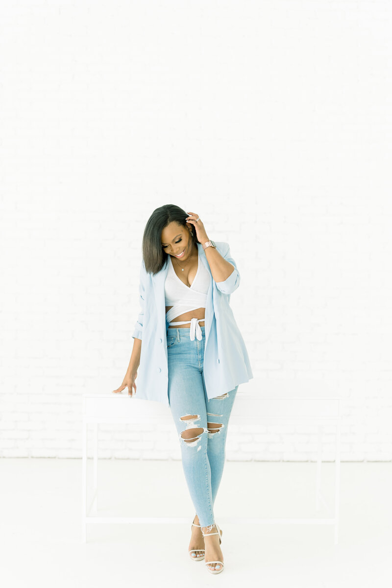 african american woman in pink jacket smiling while leaning on a white wall