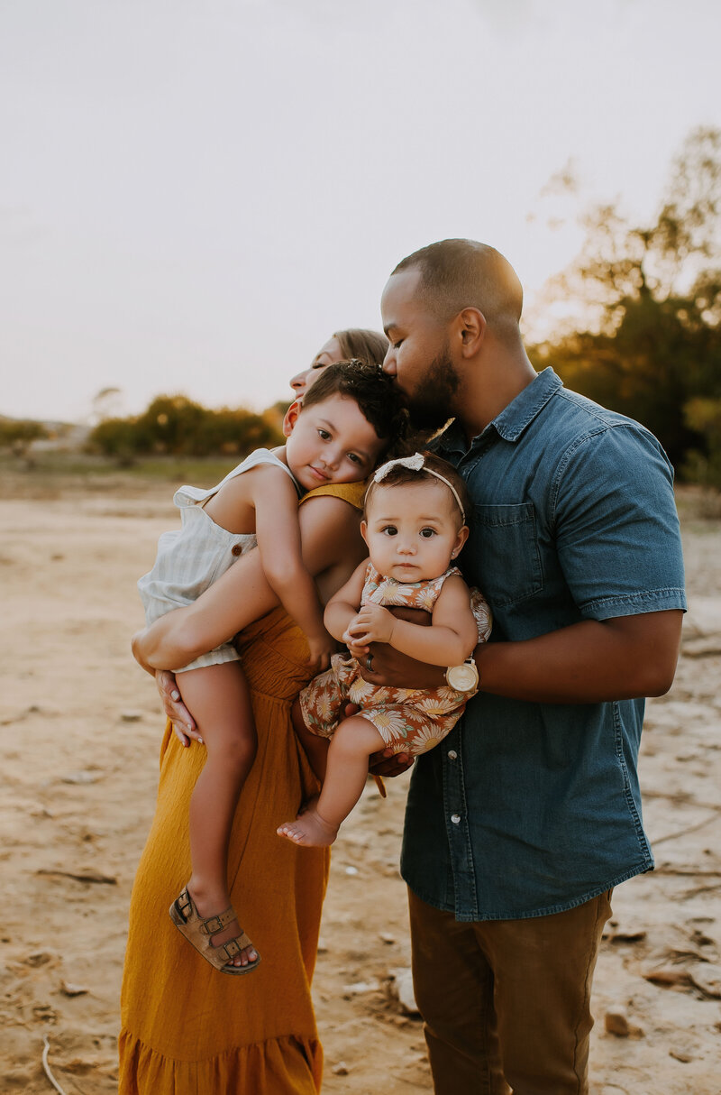 A mixed race family of four standing next to grapevine lake at murrell Park snuggling and loving on one another.