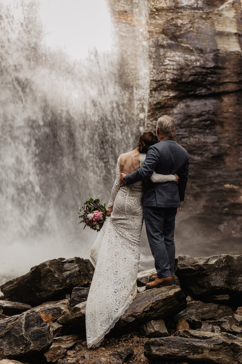 Couple standing at base of waterfall in adventure elopement