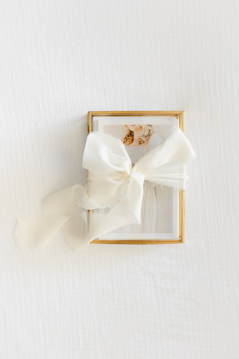 A glass box of prints tied with a white bow on top by DC Newborn Photographer