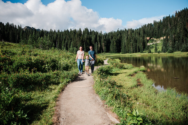Young mom with her toddler son sitting on a wooden step along a trail at Tipsoo Lake with tall pine trees in the background