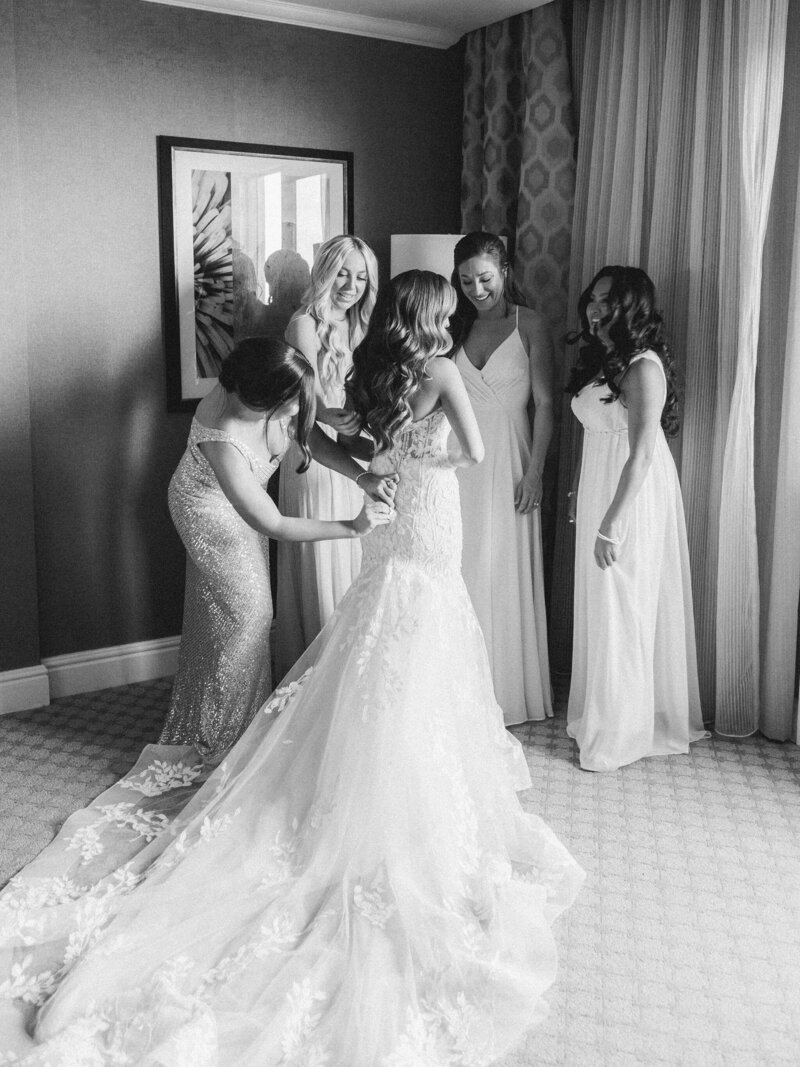 bride putting on wedding dress while surrounded by bridesmaids