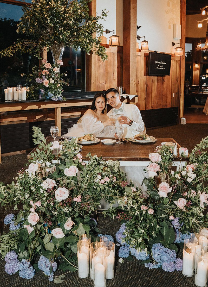 Couple sitting and posing at their wedding table, surrounded by flowers and candles at Mountain Creek Resort.