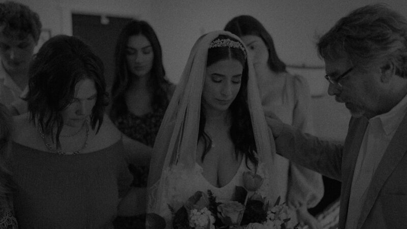 person in wedding dress praying surrounded by five people