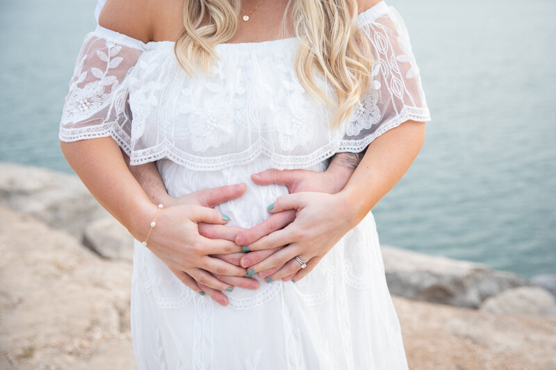 An Austin wedding photographer captures a pregnant couple holding hands in front of the ocean.