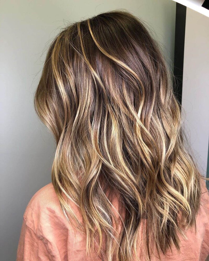 A back view of a woman with soft, slightly curled blonde hair, showcasing a beautiful styled look by 212 Salon, Spa, & Barbershop