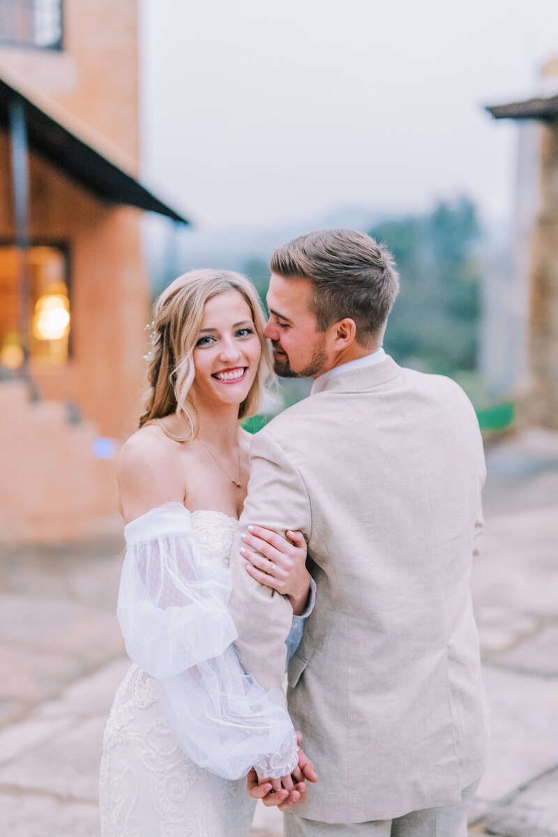 Couple with their arms interlocking and man looking at woman while woman smiles at the camera