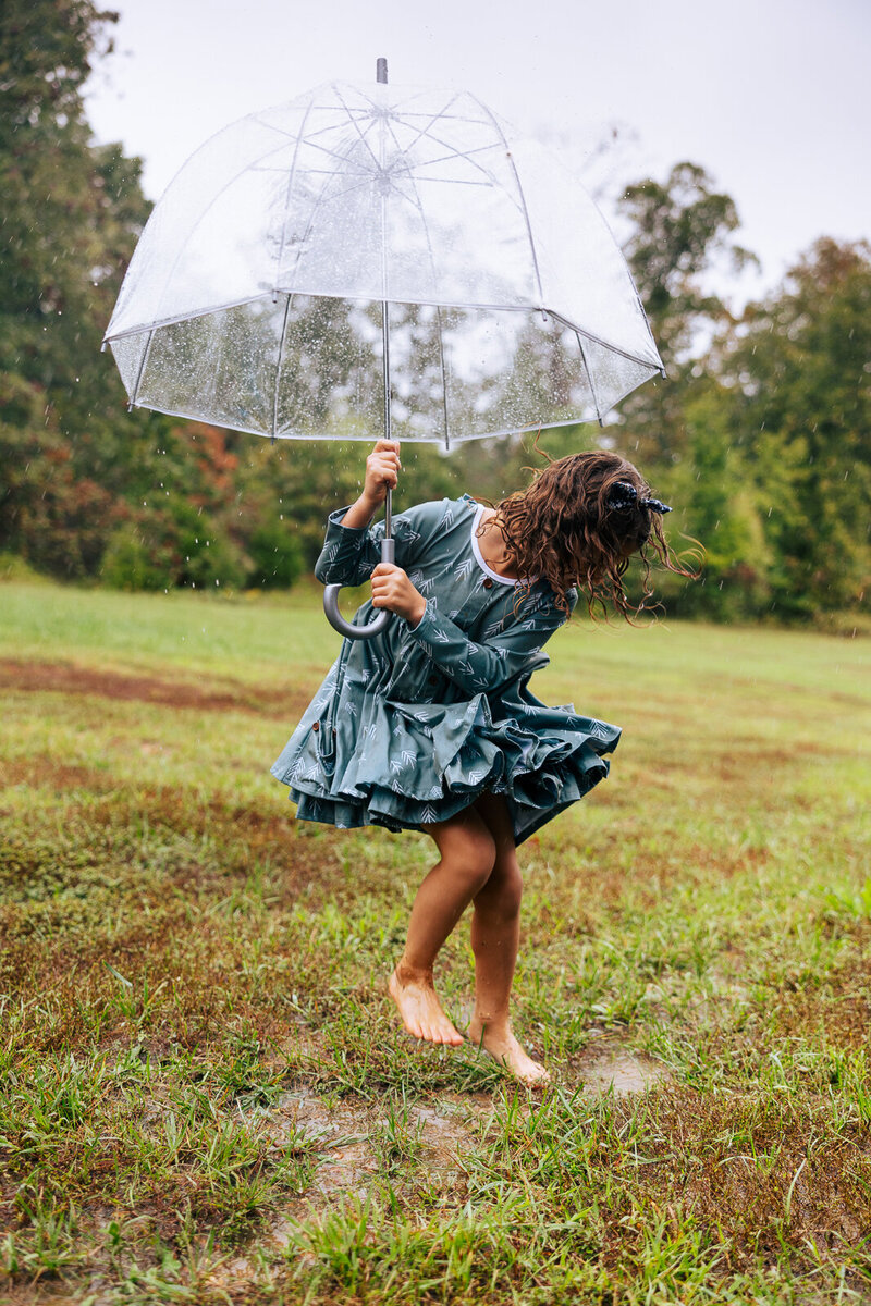 Little girl holding umbrella and jumping in a puddle. 