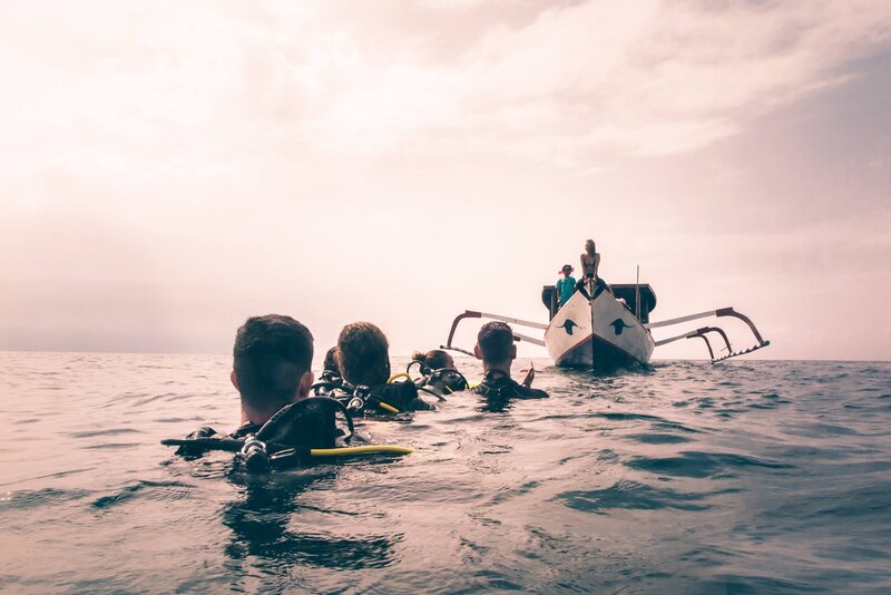 Scuba divers lined up in the water with heads above surface looking at the scuba diving boat coming to pick them up, sunsetting is pink