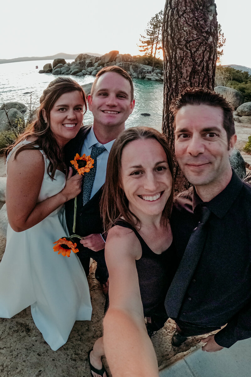 Lake Tahoe elopement photographer Kristin Smith and her husband Rick taking a joyful selfie with a newly married couple at sunset along the lake’s rocky shoreline.