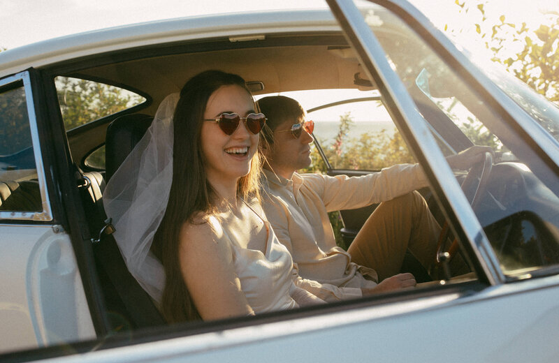 Newlyweds in heart-shaped sunglasses ride off in a vintage car at golden hour, perfectly blending retro vibes with modern Seattle wedding photography.