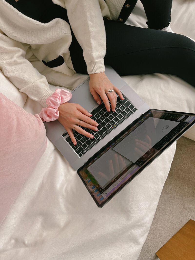 Overhead shot of hands typing on a grey laptop with a pink scrunchie on one wrist.