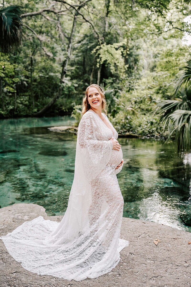 Pregnant mom in long white gown standing on a rock at Kelly Rock Springs in Orlando