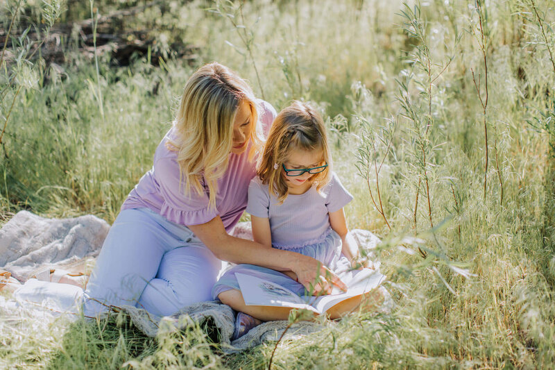 little girl reading a book while mother points to words