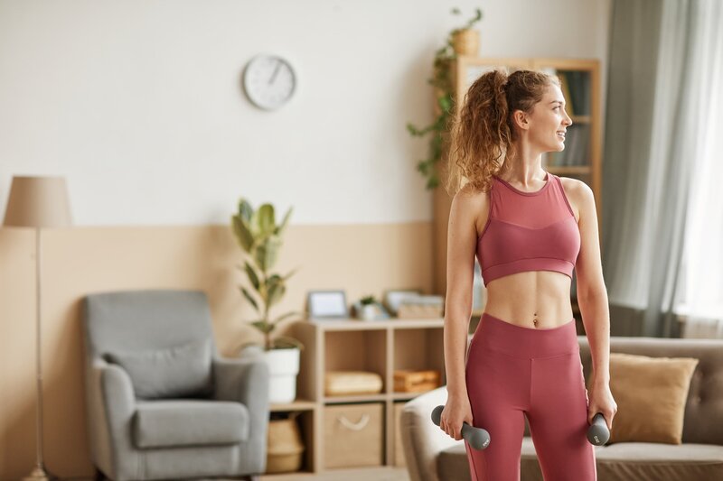 Femme souriante en tenue d'entraînement avec des poids – physiothérapie à Montréal pour soulager la douleur, retrouver sa mobilité et reprendre ses activités avec autonomie
