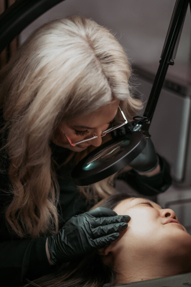 Skincare specialist examining her client's skin for acne in her Appleton beauty studio.