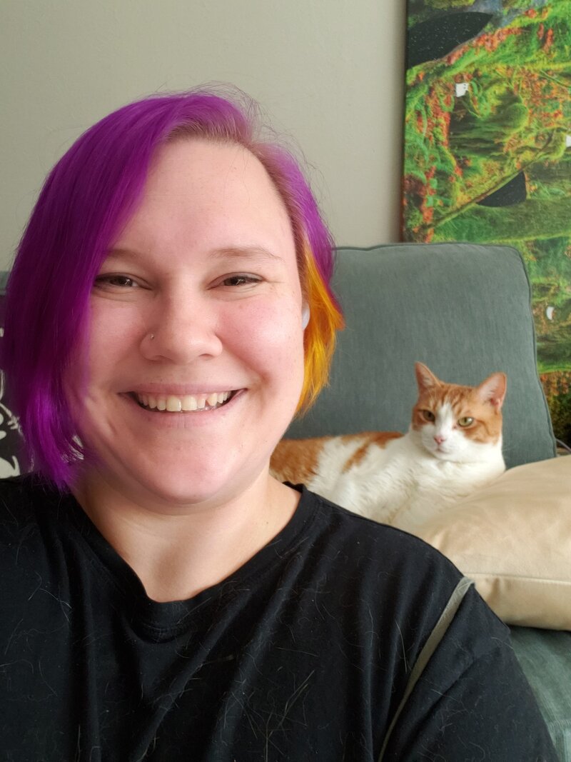 Women in golden light, wearing dark rimmed glasses and striped shirt, smiling down at her hands as she rolls out clay