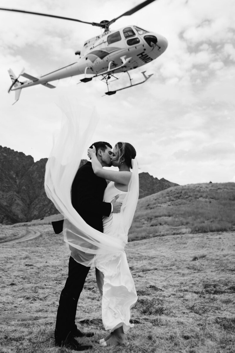 The Lovers Elopement Co - bride and groom kiss at wedding elopement on mountain top with helicopter taking off in the background