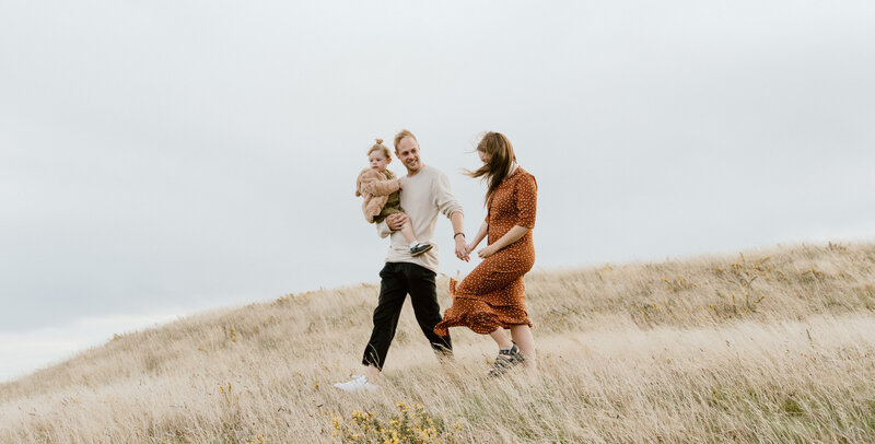 mom, dad, and baby smiling in field for family portraits