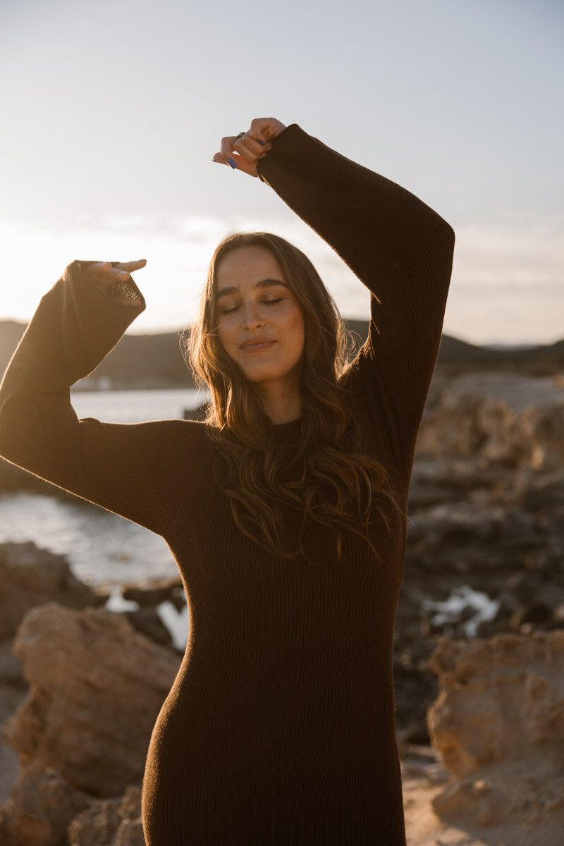 A woma is dancing on the beach for a shoot during sunset on Ibiza.