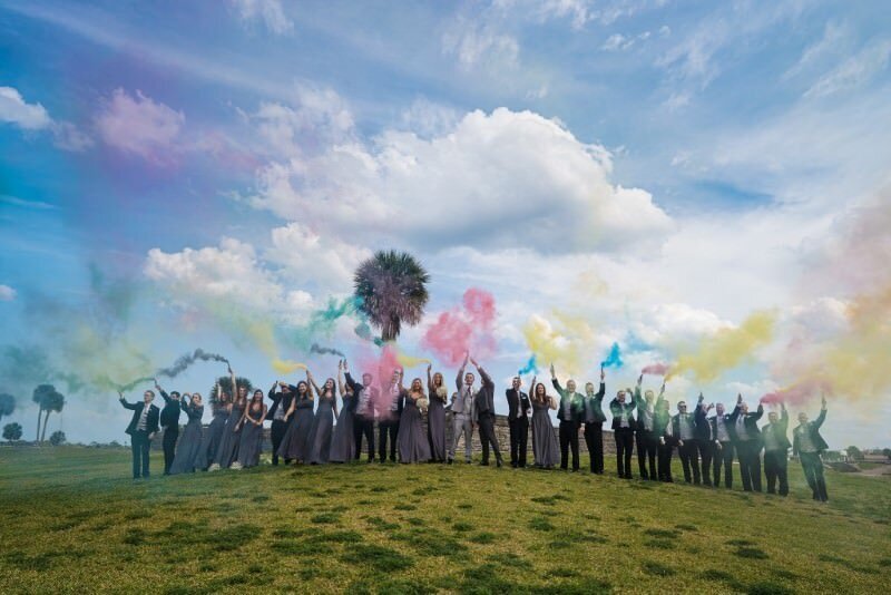 a large wedding party celebrate with a blue sky and white puffy clouds