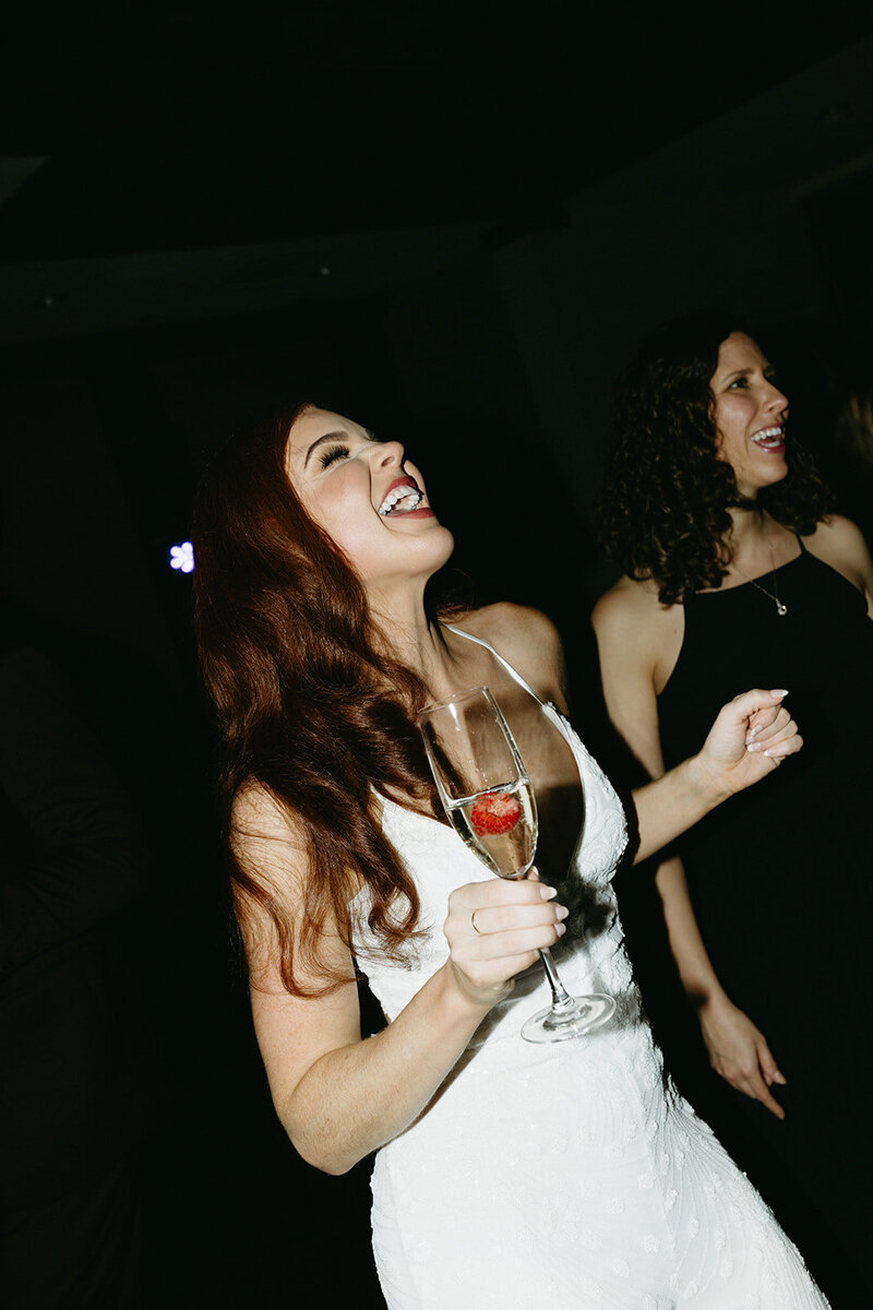 Flash photo of bride dancing and holding a glass of champagne