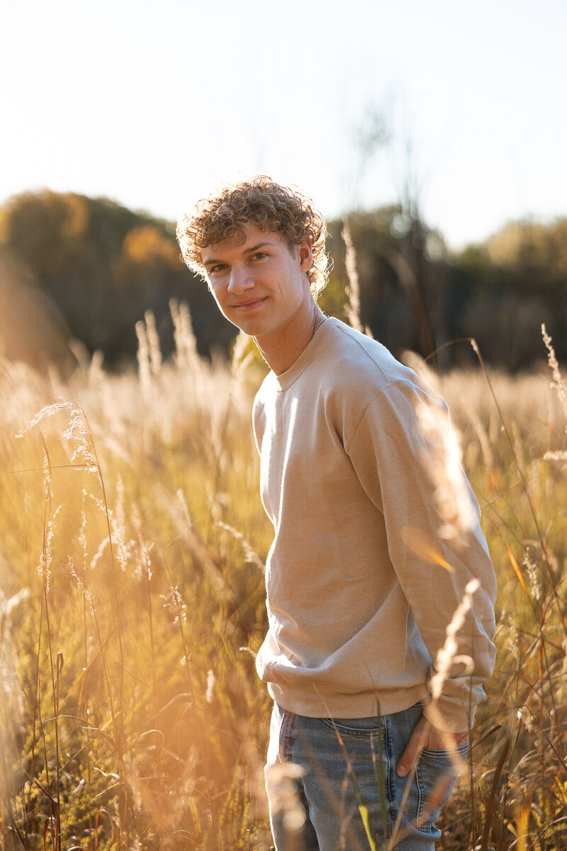 Senior boy standing in tall golden grass at sunset in Farmington, Missouri. 