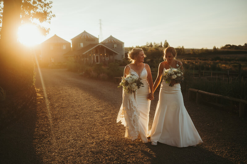 brides holding hands walking with sunset in the background