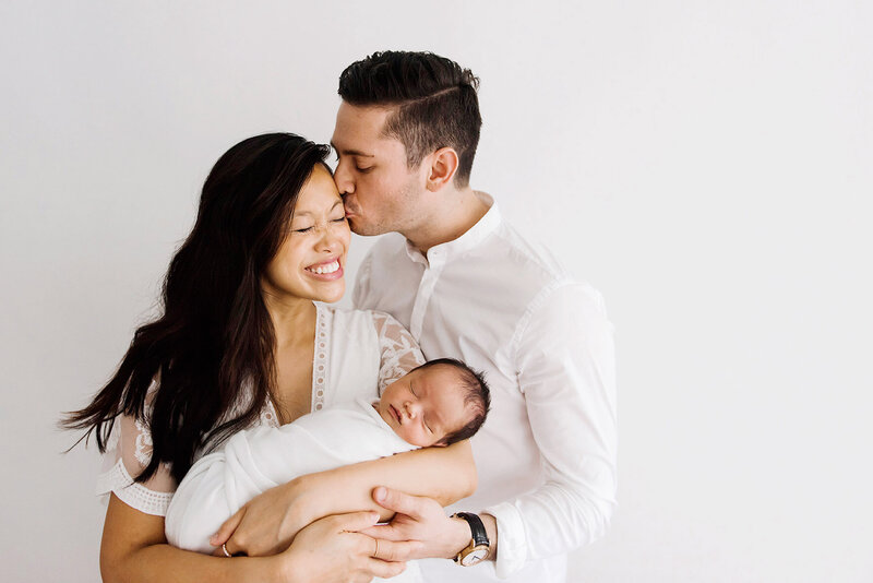 parents kissing holding newborn baby taken by boston photographer​
