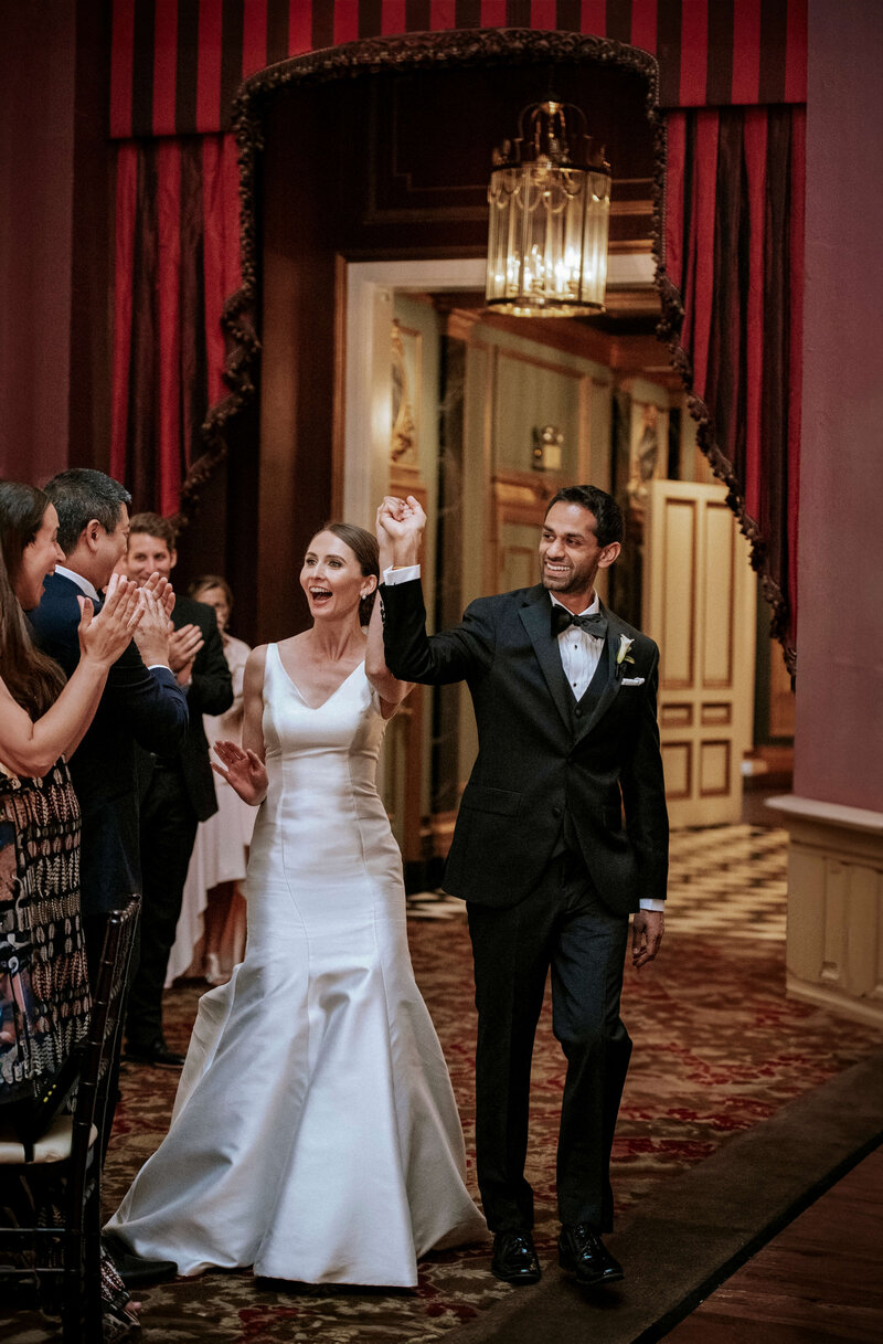 elated-newlyweds-entering-ornate-ballroom-to-cheering-guests