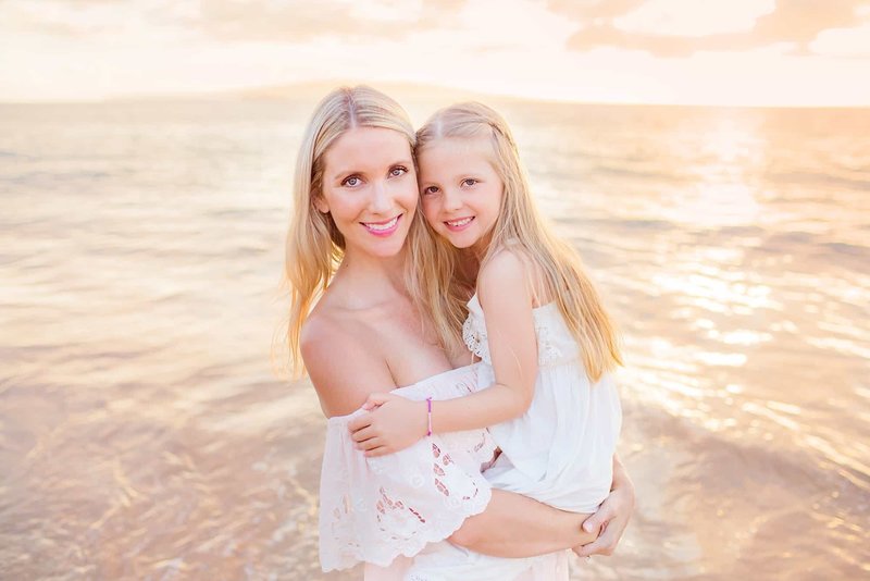 Blonde woman in white off-shoulder dress holds her daughter for a mother daughter portrait in Hawaii