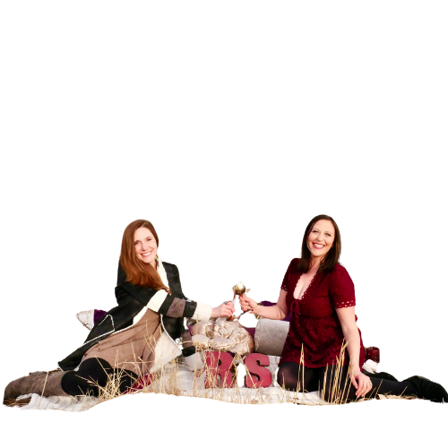 Ritual Sisters, Michelle and Kelly, sitting amongst colorful pillow smiling widely at the camera while holding their gold goblets in a cheers