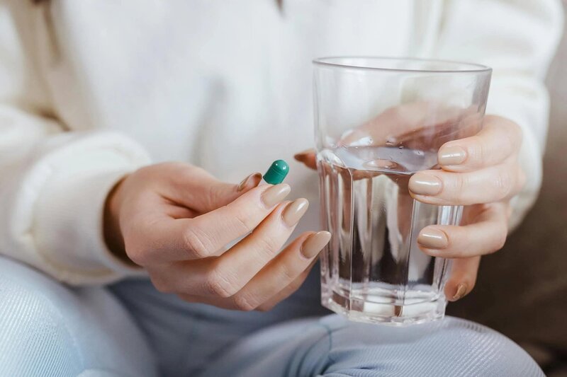 photo of a person holding medicine in one hand an a cup of water in the other hand