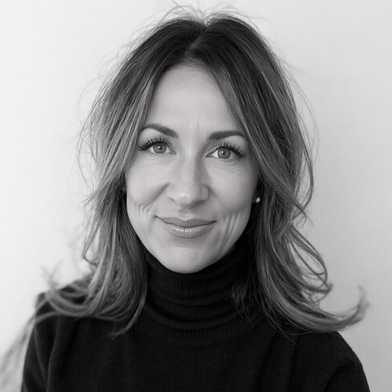 A woman with shoulder-length hair wearing a black turtleneck sweater smiles at the camera against a plain background. The black and white photo captures the creative spirit behind Sweet Pea Ink Creative’s brand design expertise and Cristina Horvath, the CEO.