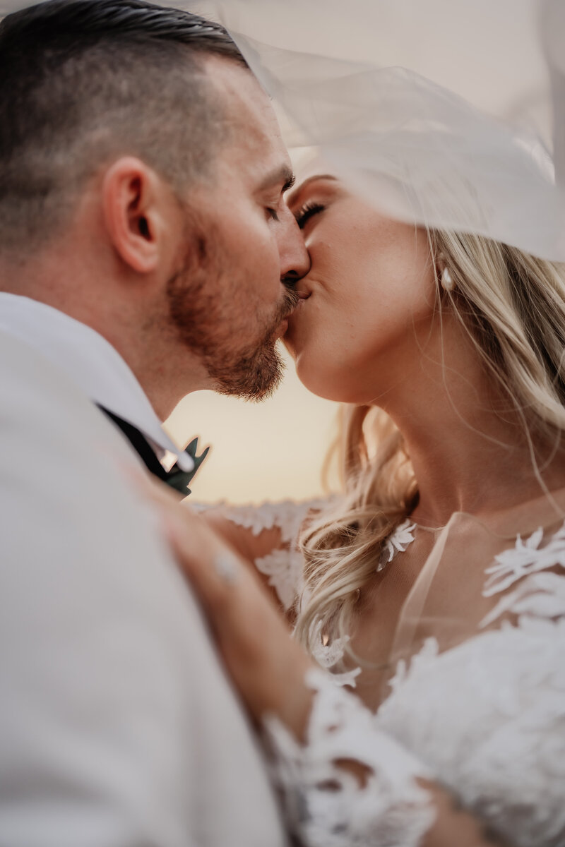 Family Photographer, a bride and a groom kiss , she is in her wedding dress, he is in a white tux