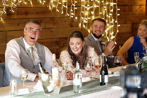 bride and father of bride sitting at the top table at the bride's wedding laughing at a joke the best man told during his speech