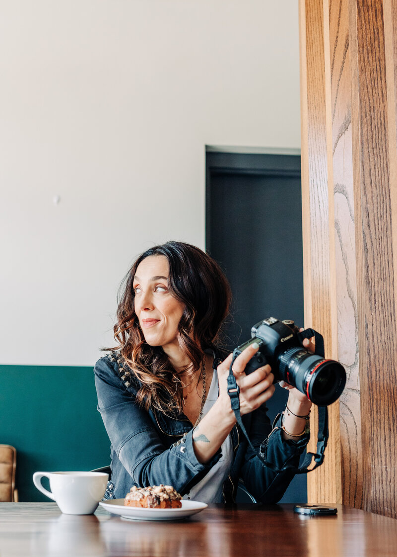 Headshot photo of Maria Riboli relaxing with coffee and pastry while looking at a photoshoot on her camera