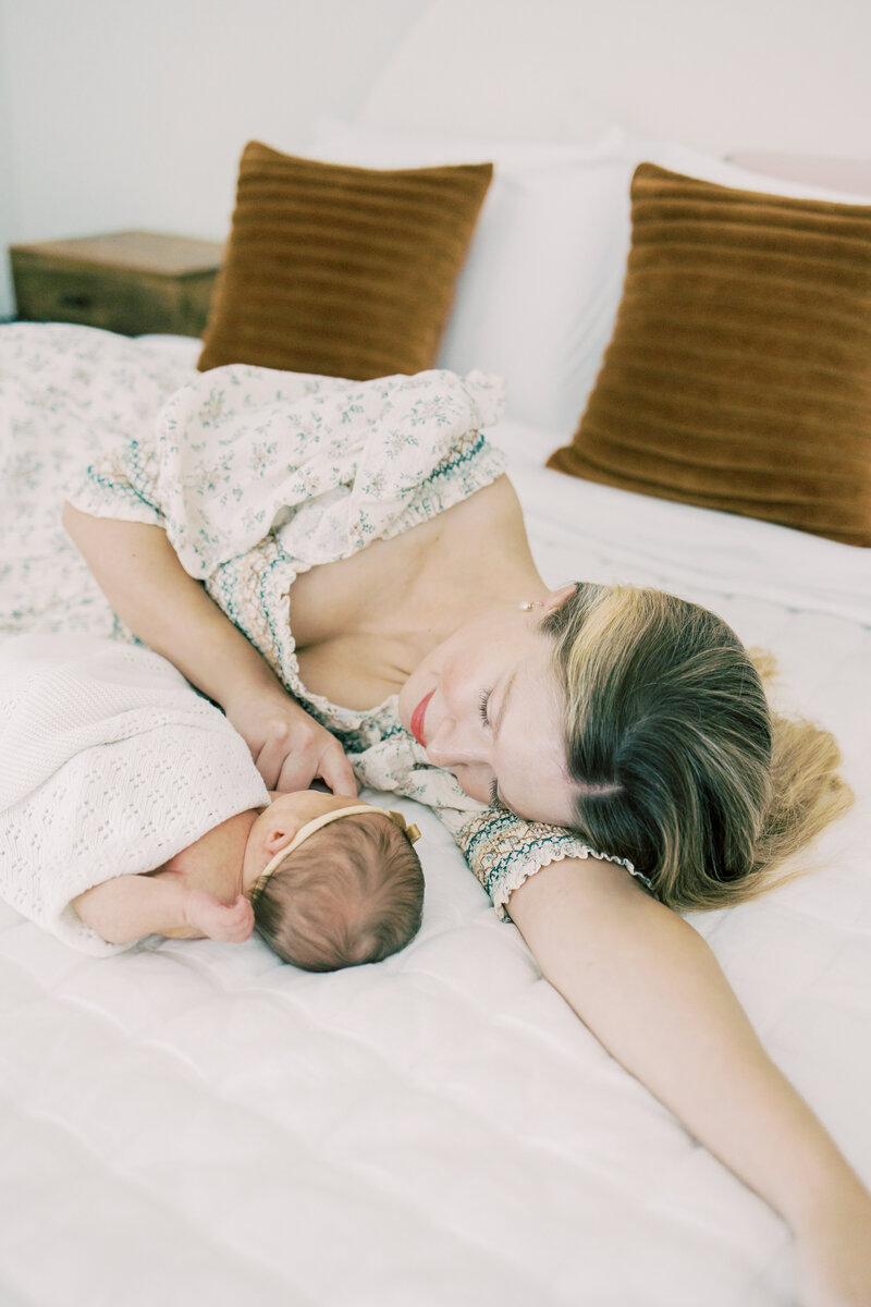 Austin newborn mom smiles at her baby laying on the bed.