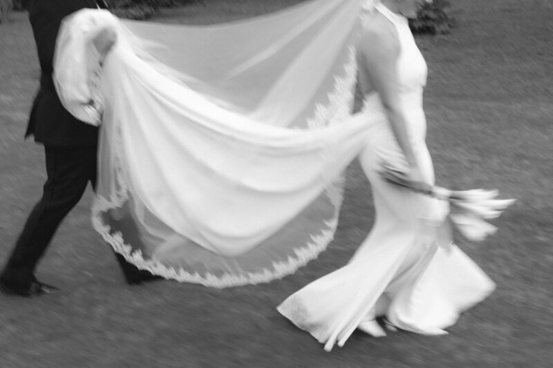 Black and white motion-blur image of bride and groom walking through a field at Nashville wedding
