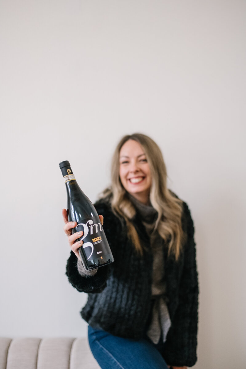 Sammy in a black coat holding up a black champagne bottle