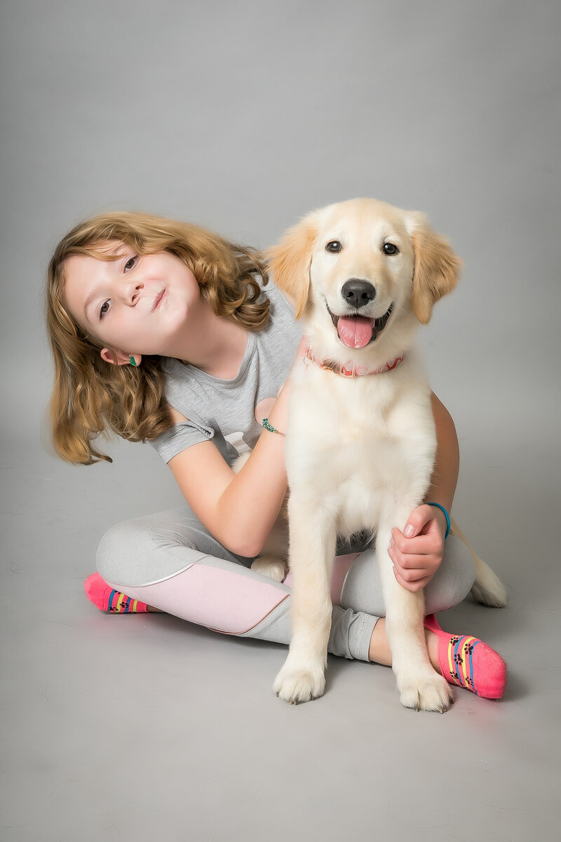Golden retriever puppy and child sit together to have photos taken in modern Sacramento studio