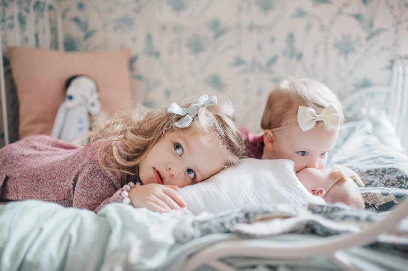 Little girl laying next to a baby on a bed