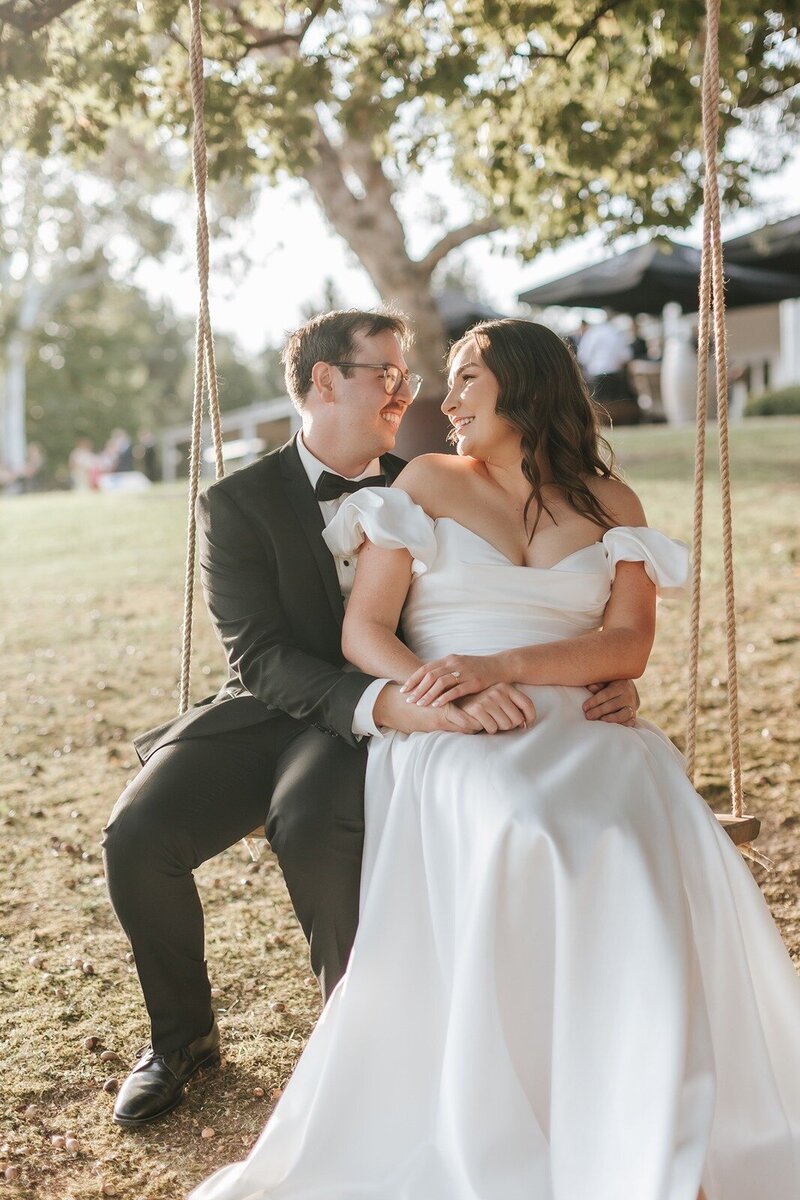 A bride and groom hugging and sitting on a wooden swing.