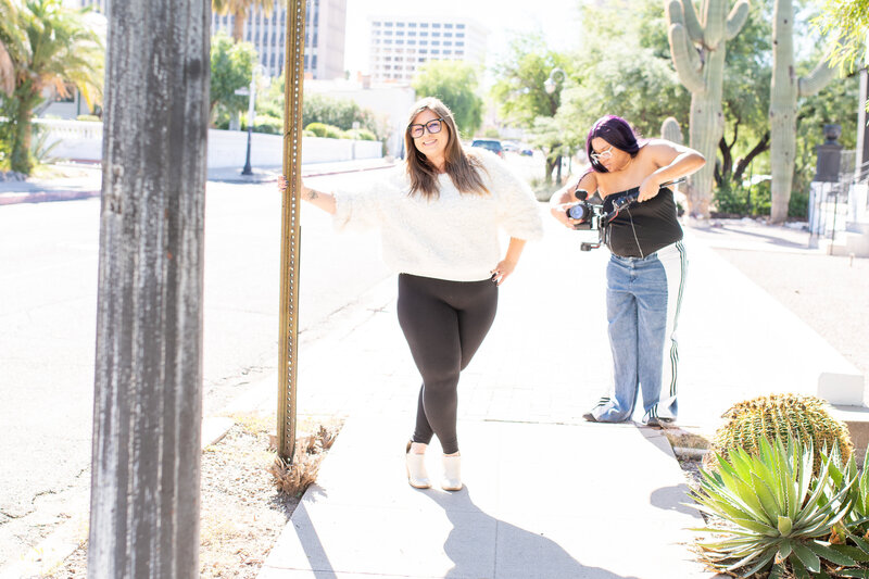 Smiling woman wearing glasses and a cozy white sweater standing on a sunny Tucson street, photographed by Vyrl Photo, showcasing Tucson brand photography.