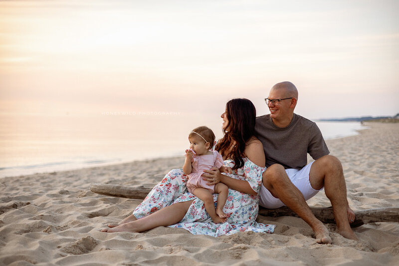 A family of four sitting on the sand at a West Michigan beach during sunset, sharing a warm and intimate moment during a lifestyle family photography session.
